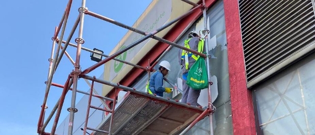 Técnicos sobre andamio limpiando la fachada de vidrio de un local comercial